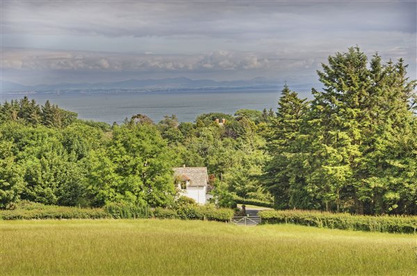 Cottage with field in front, trees behind and sea views with England in the distance